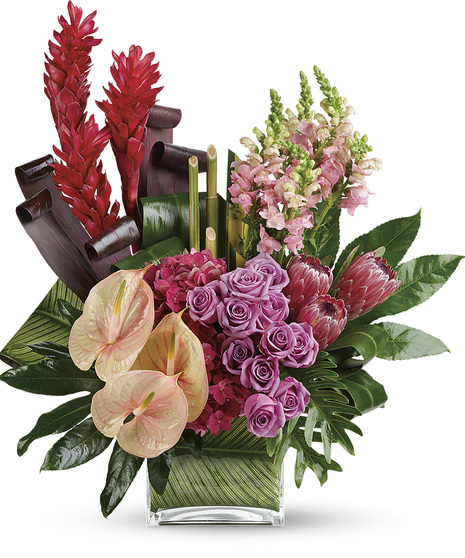 Bouquet of mixed tropical flowers and greenery in a leaf-lined glass cube vase