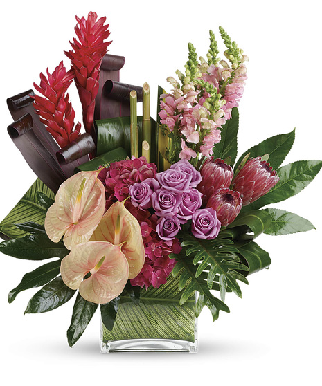 Bouquet of mixed tropical flowers and greenery in a leaf-lined glass cube vase